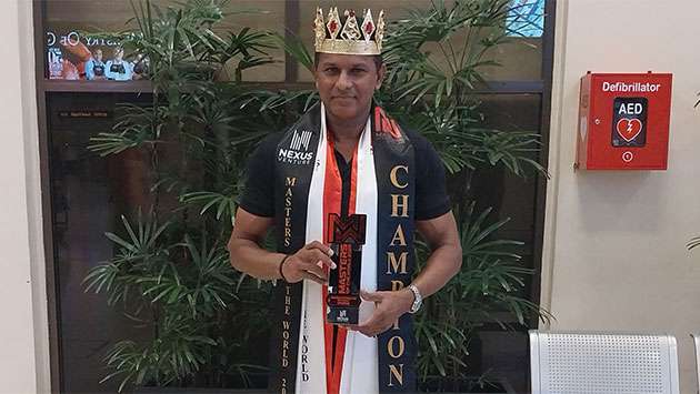 A distinguished Sri Lankan gentleman in formal attire standing on an international pageant stage under warm lights