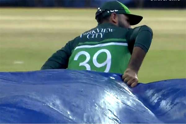 Fakhar Zaman helps groundstaff cover the field after rain stops play in Colombo