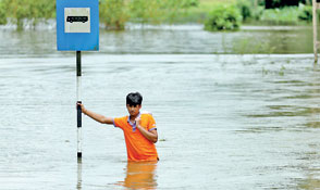 A man holds a bus stop post on a flooded road as he waits for a military vehicle to go to a town